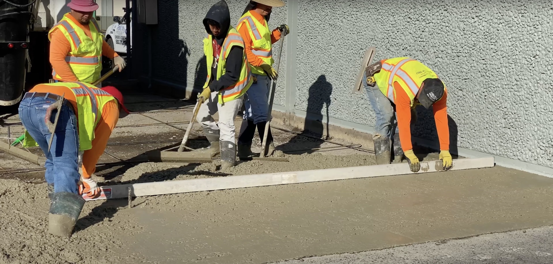 Professional concrete finishing crew using screeds and hand tools for smooth surface completion