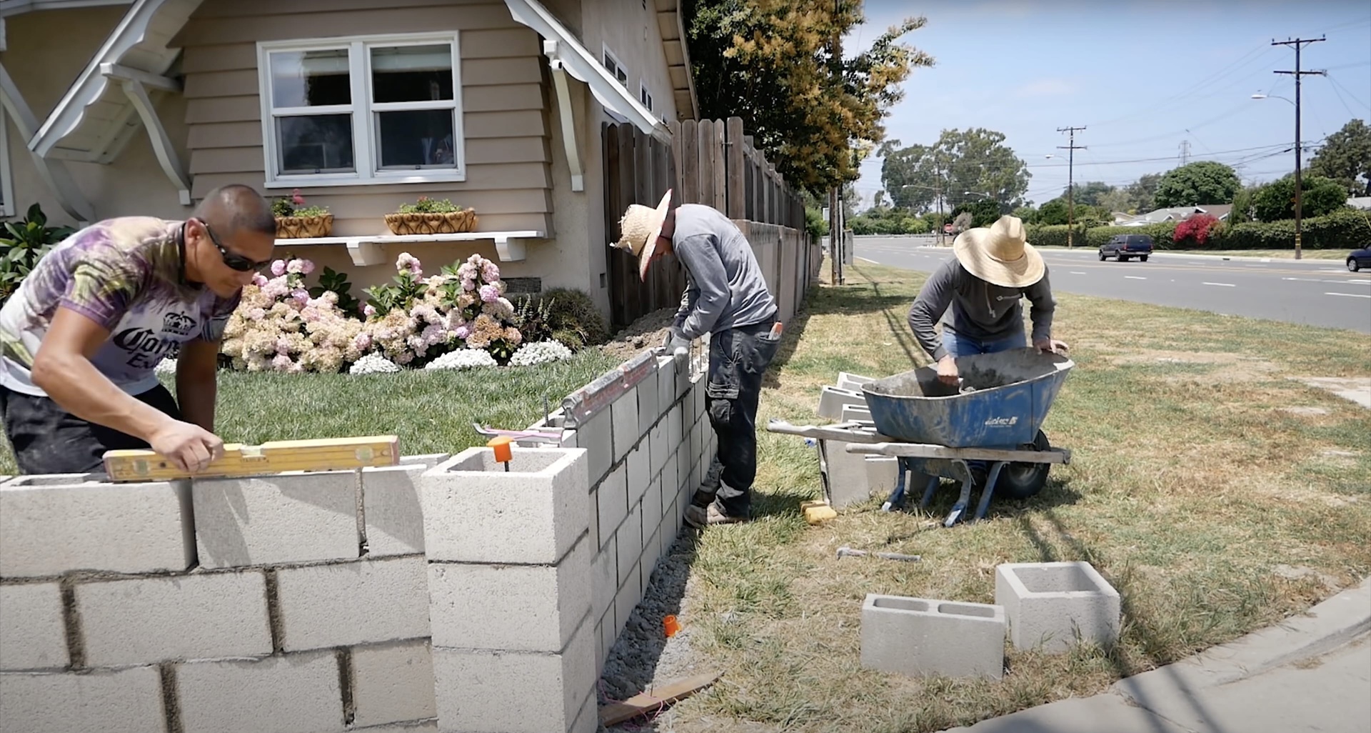 Skilled concrete workers building decorative concrete block retaining wall with proper leveling techniques